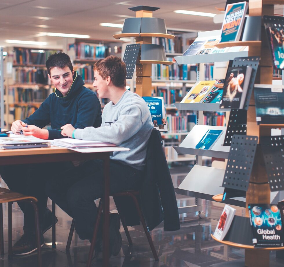 2 studenten overleggen in de bibliotheek